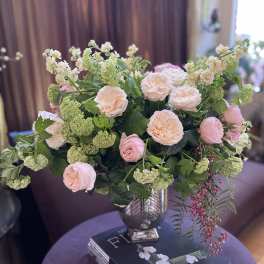 Blush roses and pale green flowers arranged in a glass vase on a table