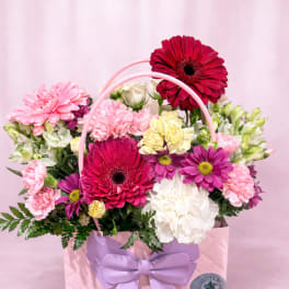 Pink gift bag filled with mixed flowers and a lavender bow