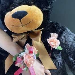 Black teddy bear with a gold bow and pink floral wrist corsage