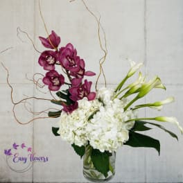 White hydrangeas and purple orchids in a clear glass vase with curly branches