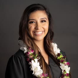 Woman wearing a white and purple orchid lei over a black graduation gown