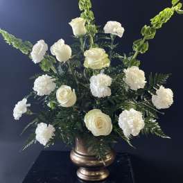 White roses and carnations in a bronze vase with tall green spikes