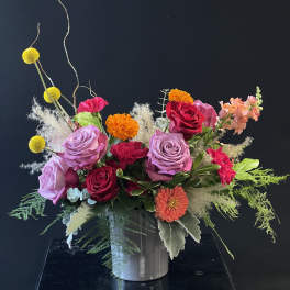 Mixed bouquet of roses, carnations, and orange blooms in a gray vase