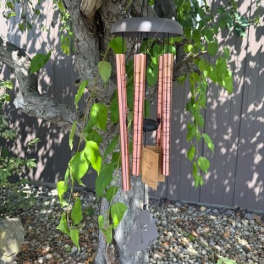 Copper wind chime hanging from a tree branch