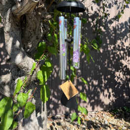 Black wind chime hanging from a tree branch outdoors