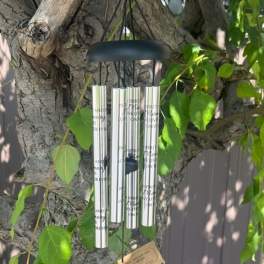 Silver wind chime hanging from a tree branch with green leaves