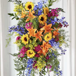 Colorful standing floral spray with sunflowers, lilies, and blue flowers