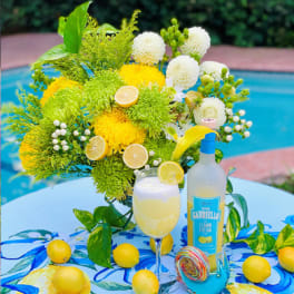 Yellow and white floral arrangement with lemons and a bottle on a table