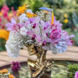 Mixed bouquet with orchids, roses, hydrangeas, and baby's breath in a gold vase