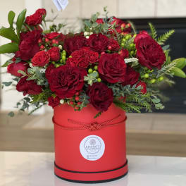 Red roses arranged in a red round box with greenery