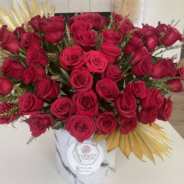 Large bouquet of red roses in a white marble-patterned box with gold accents.