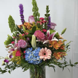 Tall mixed bouquet in a clear glass vase with pink, purple, blue, and orange flowers