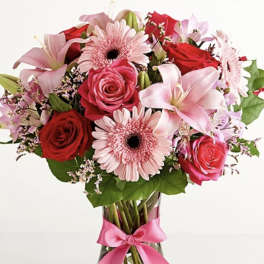 Bouquet of pink and red flowers in a glass vase with a pink ribbon