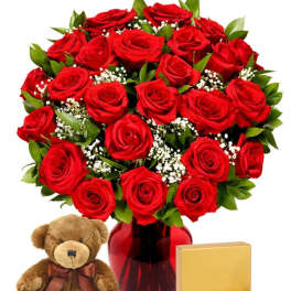 Red roses in a vase with a teddy bear, chocolates, and a gift box