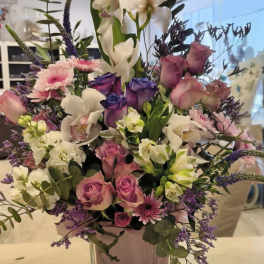 Mixed bouquet of white orchids, pink roses, and purple flowers in a glass vase