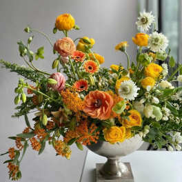 Mixed orange, yellow, white, and peach flowers in a silver pedestal vase
