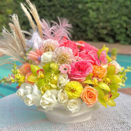 Colorful floral arrangement in a white bowl vase with feathers