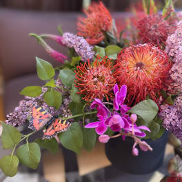 Bouquet of orange pincushion blooms and purple flowers with a butterfly accent
