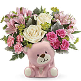 Pink teddy bear holding a bouquet of pink and white flowers