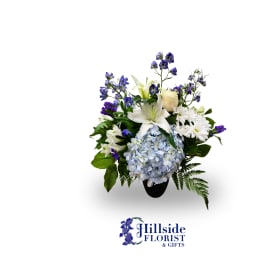 White lilies, blue hydrangea, and purple flowers in a black vase