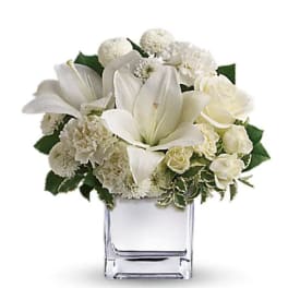 White lilies and roses arranged in a clear square vase