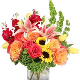 Mixed bouquet of roses, lilies, sunflowers, and tulips in a glass vase