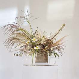 Wildflower arrangement with white daisies and tall grasses in a neutral vase