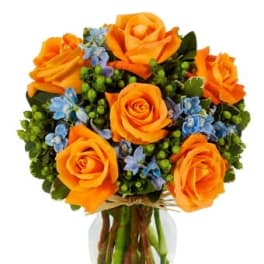 Round bouquet of orange roses with small blue flowers in a clear glass vase