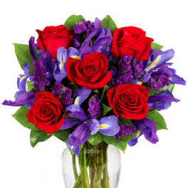Clear glass vase of red roses mixed with purple irises and small violet flowers