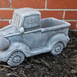 Gray pickup truck-shaped planter against a brick wall