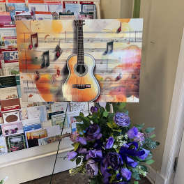 Purple floral standing spray with ribbon beside a guitar display
