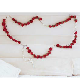 Red rose garland draped across a white couch with a hanging cross