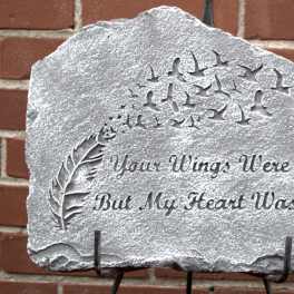 Gray stone memorial plaque with carved birds, a feather, and the inscription 'Your Wings Were Ready, But My Heart Was Not.'