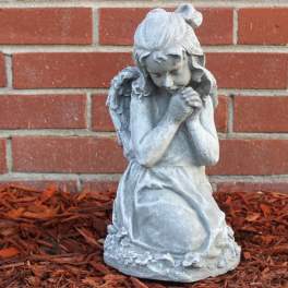 Gray praying angel statue in front of a brick wall