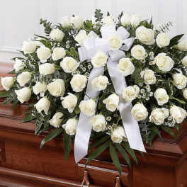 White rose casket spray with a white ribbon on a wooden casket