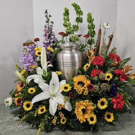 Funeral urn surrounded by a colorful floral tribute with lilies, sunflowers, and carnations