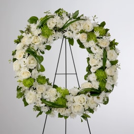 White floral wreath on a black stand with green accents