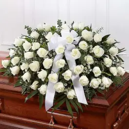 White rose casket spray with a white ribbon on a wooden casket