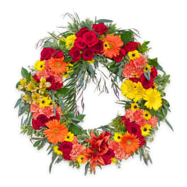 Circular floral wreath with red roses, orange gerberas, and yellow daisies
