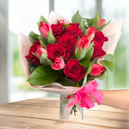 Bouquet of red roses and pink tulips wrapped in pale paper with a pink ribbon