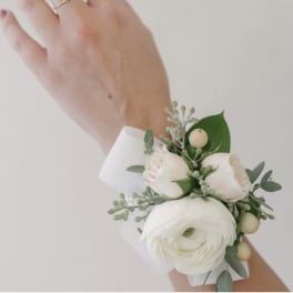 White and blush floral wrist corsage on a white band worn on the wrist.