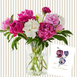 Pink and white peonies in a clear glass vase with a greeting card.