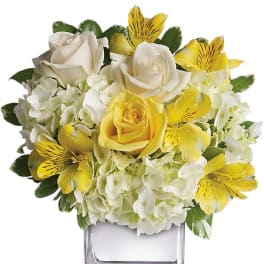 Yellow and white floral arrangement in a clear square vase
