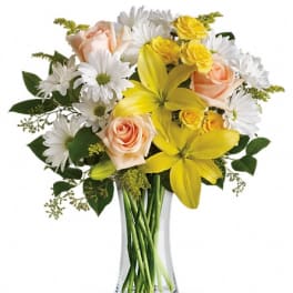 Bouquet of yellow lilies, peach roses, and white daisies in a glass vase