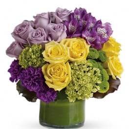 Bouquet of lavender, yellow, and purple flowers in a green glass vase