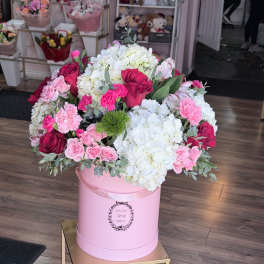 Pink and white flower arrangement in a round pink box