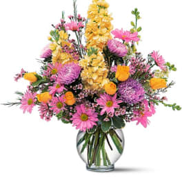 Pink and yellow mixed flowers arranged in a clear glass vase