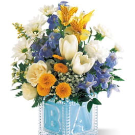 Mixed bouquet in a blue glass block vase with white, yellow, and blue flowers.
