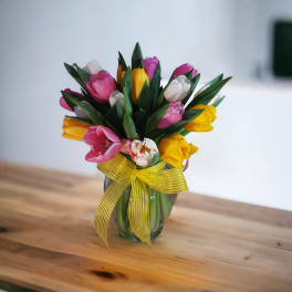 Bouquet of pink, yellow, and white tulips in a glass vase with a yellow ribbon