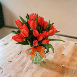 Bouquet of orange tulips in a clear glass vase with an orange ribbon